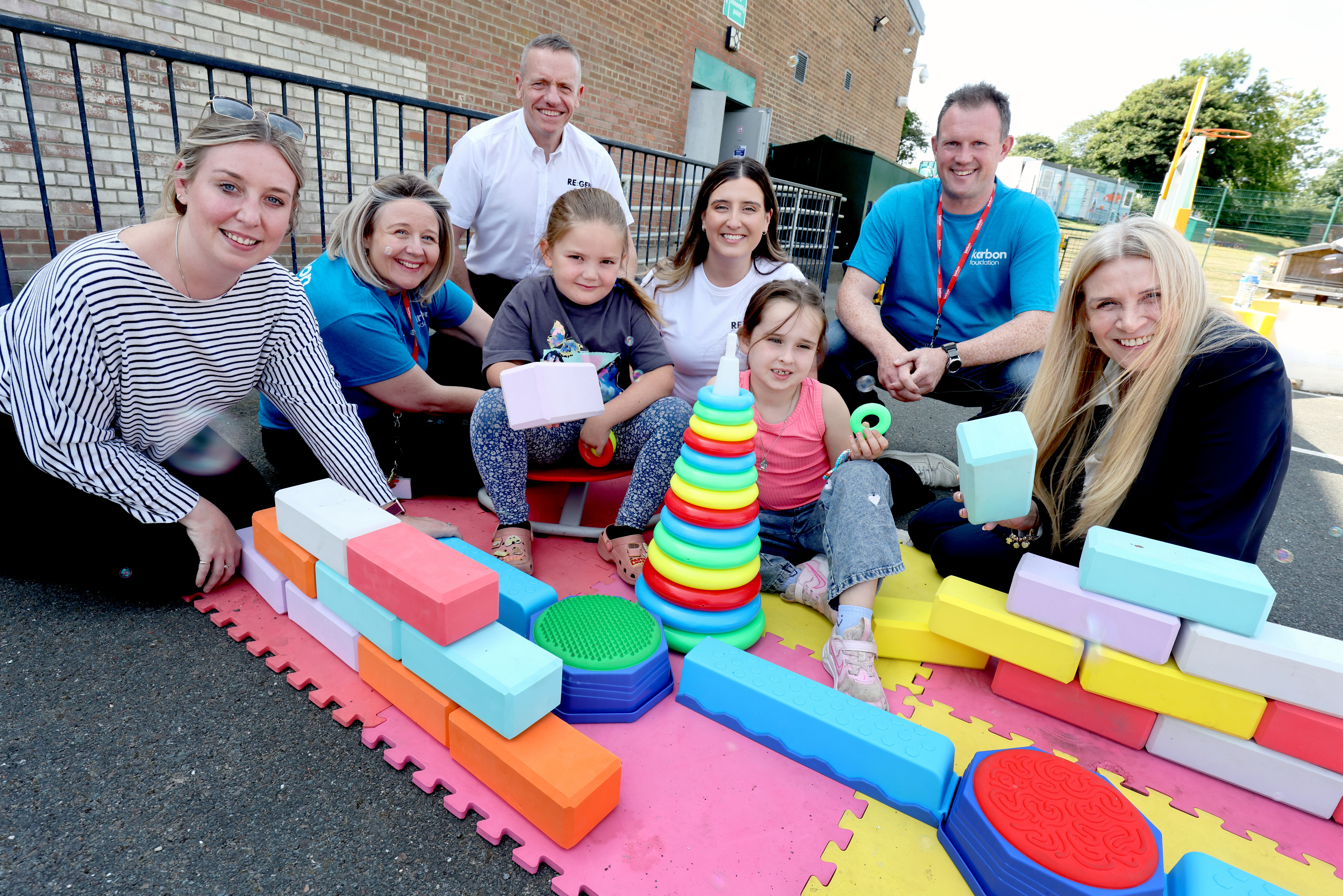 Group of adults and children sit around some toys for a photo celebrating local donations to support a summer camp in country durham